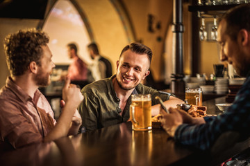 Cheerful friends drinking draft beer in a pub