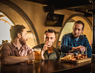 Cheerful friends drinking draft beer in a pub