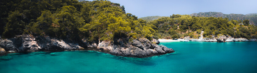 Secluded beach surrounded by valley cliffs in a tranquil bay with turquoise water and sailing boats at sunrise, Oludeniz, Turkey panoramic