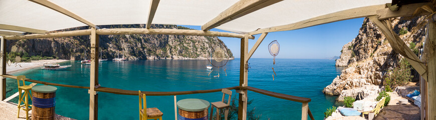 Seating area overlooking a secluded bay with turquoise water and steep valley cliffs, Oludeniz, Turkey panoramic