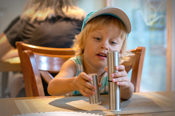 Cute little boy playin with pepper and salt shaker in restaurant