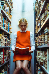 beautiful and blonde woman in orange dress reading book in library