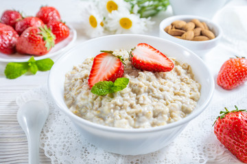 Oatmeal with strawberry and nuts in bowl on white wooden table.