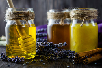 Lavender and herbal honey in glass jars with honey spoon on dark wooden background.