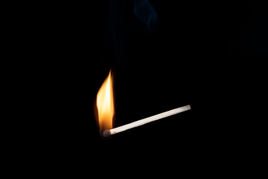 Burning wooden match with smoke over black background. Copy space