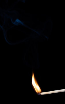 Burning wooden match with smoke over black background. Copy space
