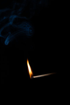 Burning wooden match with blue smoke over black background. Copy space
