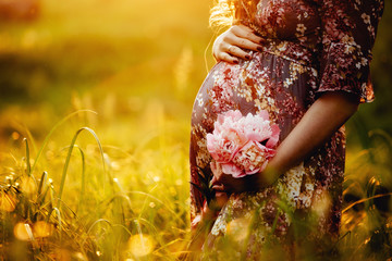 pregnant woman holding her belly and flower in the garden. - 276900379