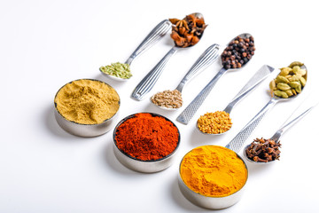 Various spices ( cumin, coriander, curry, paprika, chili, turmeric cinnamon, fenugreek, cardamom, basil leaf, parsley, cloves )  in  spoons on white background. Top view with copy space.