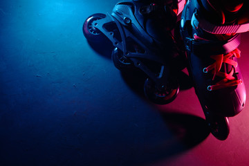 Close up view of roller skates inline skate or rollerblading on dark grunge background in neon blue magenta pink light