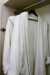 White clean bathrobe hanging on rack in hotel closet