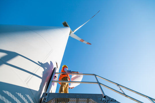 Ingegnere con gilet e caschetto fa manutenzione alla turbina eolica alta 100 metri, in montagna
