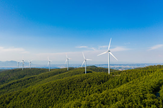 Parco eolico con turbine da 100 metri di diametro per la produzione di energia verde dal vento, su una collina con alberi. Vista aerea con drone.