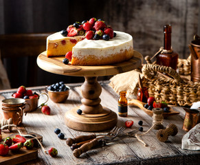 Homemade raspberry sliced biscuit cake with white cream and berries on top on wooden cake stand