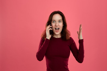Portrait of a beautiful brunette girl standing on a dark pink background and looking happy while speaking on the phone.