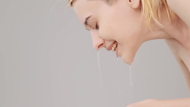 Woman washing her clean face with water. Young adult girl is  washing face with water. Slow motion. Beauty treatments. Skin care. Healthy skin concept. Profile portrait.