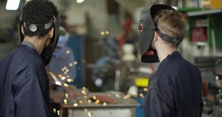 4K Young apprentice welders lifting visors & smiling at camera in workshop. Slow motion