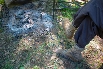 Lifestyle man with his legs crossed in the early morning in front of last night bonfire ashes