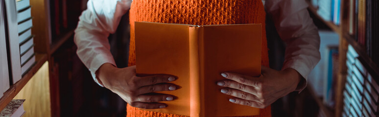 cropped view of woman holding orange book with copy space in library