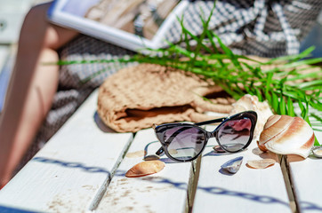 Sunglasses on a white bench, straw bag, palm leaves, shells. Beach holidays, travel, resort, eye protection