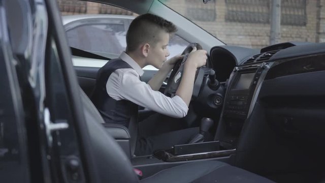 Cute little boy in business suit sitting in the car studying the salon. Child as adult.