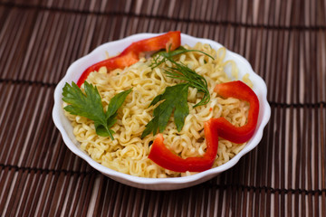 Instant noodles with red sweet peppers and greens in a white bowl. Appetizing Egg Noodles