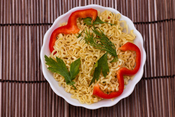 Instant noodles with red sweet peppers and greens in a white bowl. Appetizing Egg Noodles