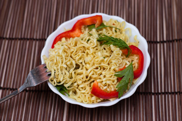Instant noodles with red sweet peppers and greens in a white bowl. Appetizing Egg Noodles