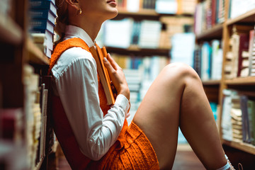 cropped view of woman in orange dress holding book in library