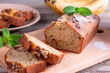 Banana bread with bananas sliced on a wooden cutting board with bananas in background