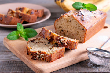 Banana bread with bananas sliced on a wooden cutting board with bananas in background