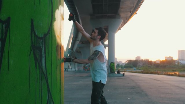 Man with spray bottle drawing colorfull graffity under the bridge at the suny day