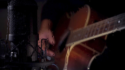 musician playing guitar at studio behind the glass with water drops