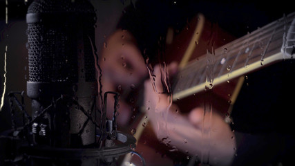 musician playing guitar at studio behind the glass with water drops