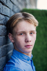 Young caucasian adult with blue eyes and blonde hair posing on black brick wall