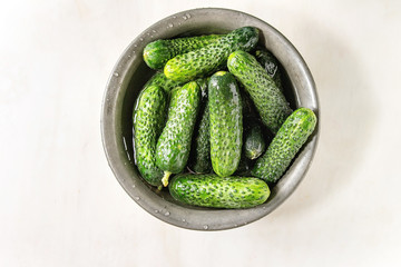 Fresh ripe organic garden cucumbers in metal bowl over white marble background. Flat lay, copy space