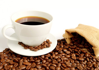 Cup of hot coffee with roasted coffee beans scattered from burlap bag on white background