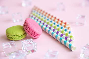 Multicolored drinking straws and macaroons with ice cubes abstract isolated on rose.