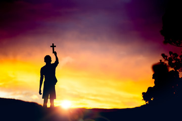 Young male standing holding christian cross for worshipping God at sunset background. christian silhouette concept.