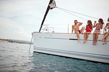 Naklejka premium vacation, travel, sea, friendship and people concept - people sitting on yacht deck.