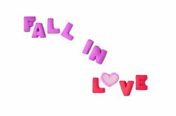 The word FALL IN LOVE spelled with purple and pink alphabet shaped biscuits and a heart shaped marshmallow candy on white background