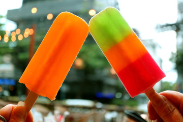 Clinking with two mix colorful popsicles against blurry urban evening view