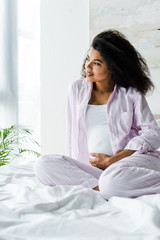 attractive pregnant african american woman touching belly on bed