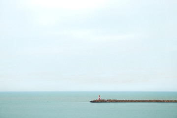 Obraz premium Lighthouse in sea on embankment. Red lighthouse on horizon background. Light tower in middle of sea. Beacon points the way. Light station on skyline
