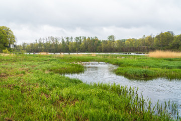rural area, a narrow section of the river in the foreground, and a wide waterfall in the distance