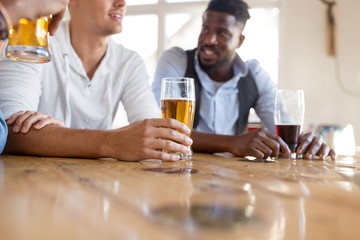leisure and drinks concept - male friends drinking beer at bar or pub