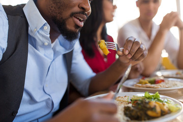 leisure, food and people concept - close up of african american man eating with friends at restaurant