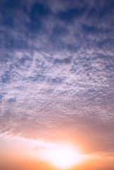 Bright sun at sunset on the background of clouds and blue sky.