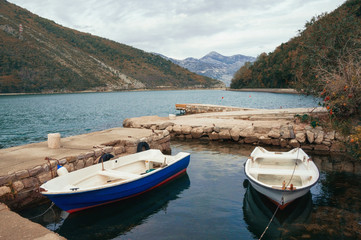 Fototapeta na wymiar Autumn landscape. Two fishing boats on the water in a small harbor on a cloudy day. Montenegro, Adriatic Sea, view of Kotor Bay near Verige Strait
