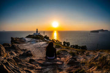 beautiful Greek sunset at the lighthouse on the island of Santorini, a woman shot from behind,...